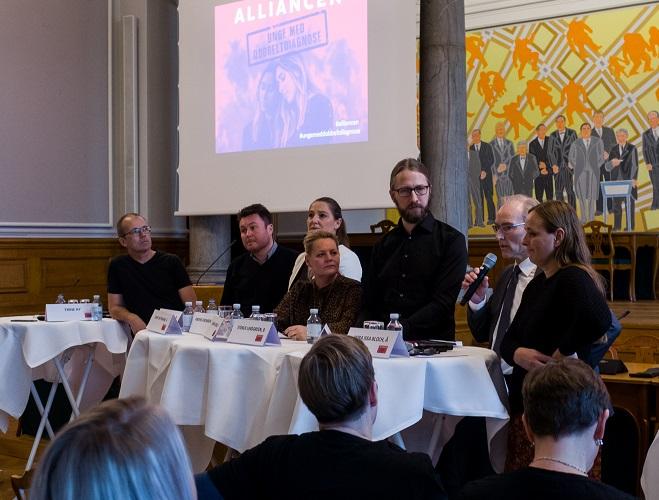 Syv personer står ved høje borde og debatterer